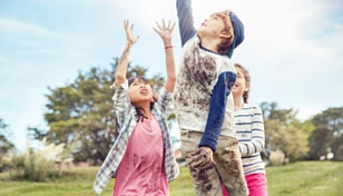 Three children covered in dirt and mud jump to try to catch a ball